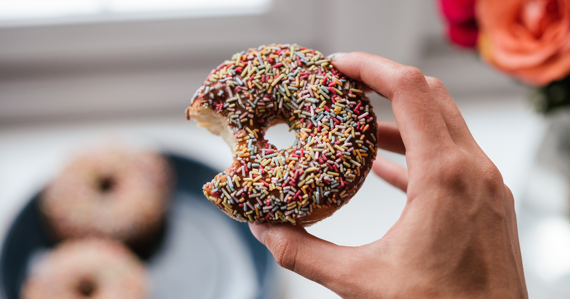 a person holding a doughnut with sprinkles on it and a bite mark taken out of it